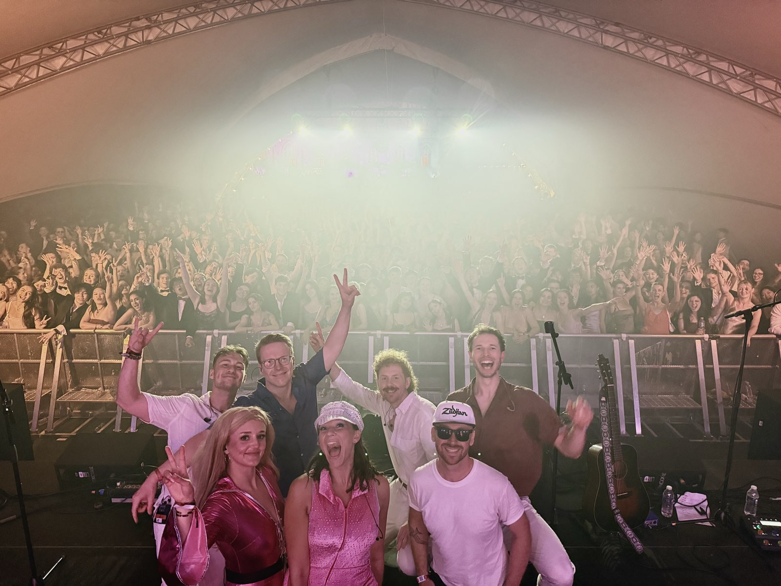 The band on stage at the end of a show with a full tent of people behind them