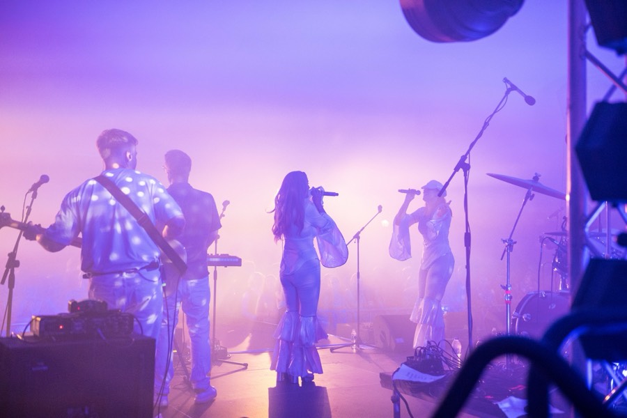 The full band mid-song, guitar and bass to one side, singers centre and drums to the right