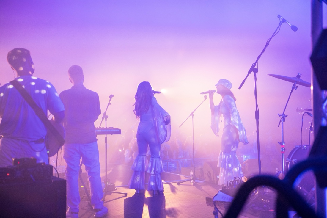 The band seen from the wings on a hazy festival stage