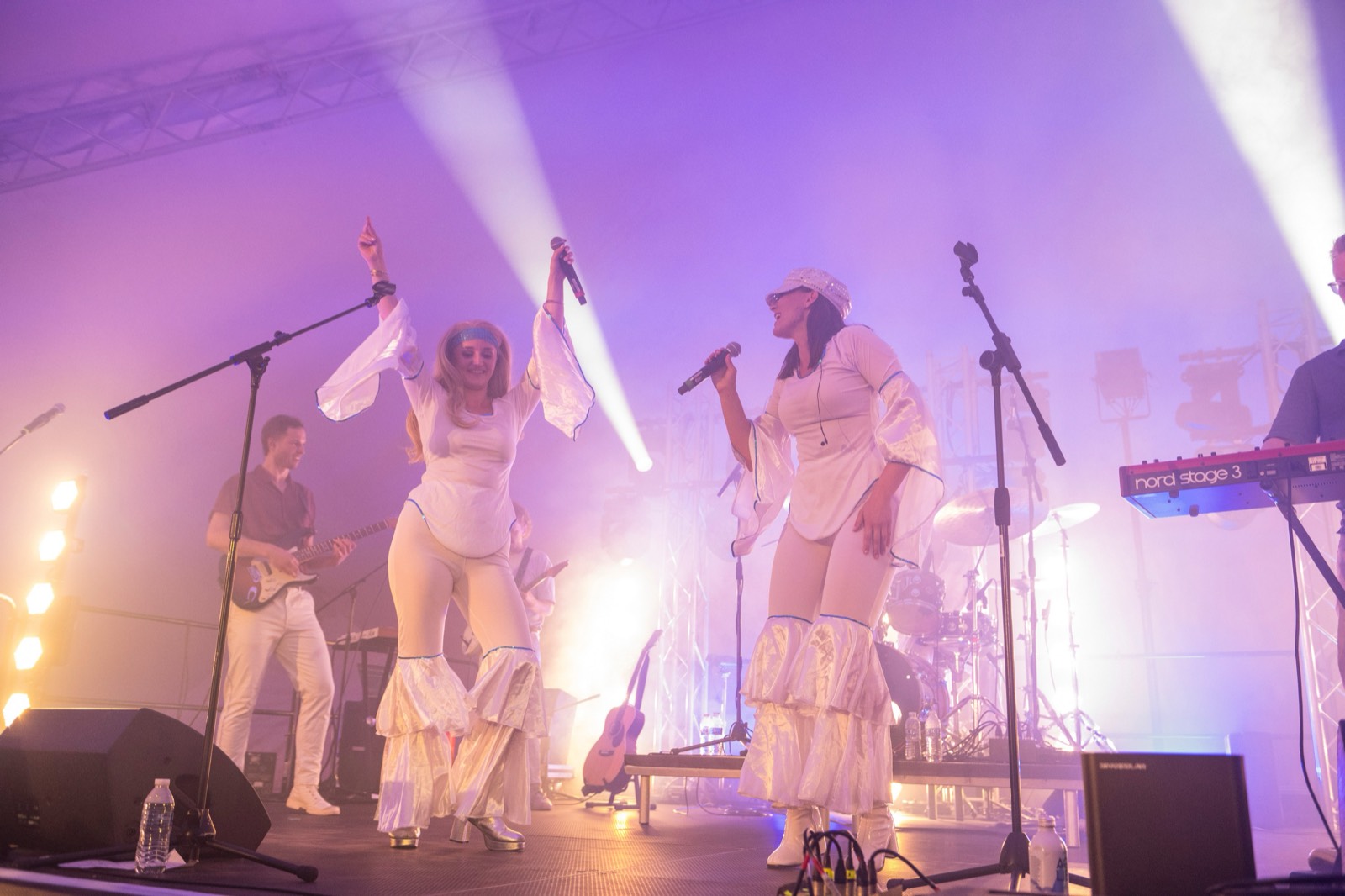 Two lead vocalists mid-song at the front of the stage with the band playing behind them